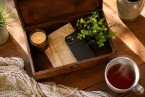 mercury retrograde survival kit shown by a small wooden box holding a candle, an old letter, and a phone face-down on a kitchen table in warm evening light