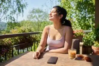 Summer habit to quit shown by a woman setting her phone face-down on a sunny table and turning toward the sunlight, choosing to quit a draining summer habit