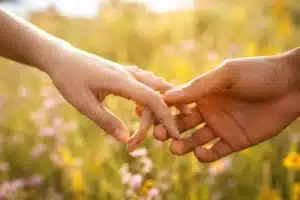 The way you fall in love shown by a close-up of two hands gently intertwining above a sunlit field of summer flowers
